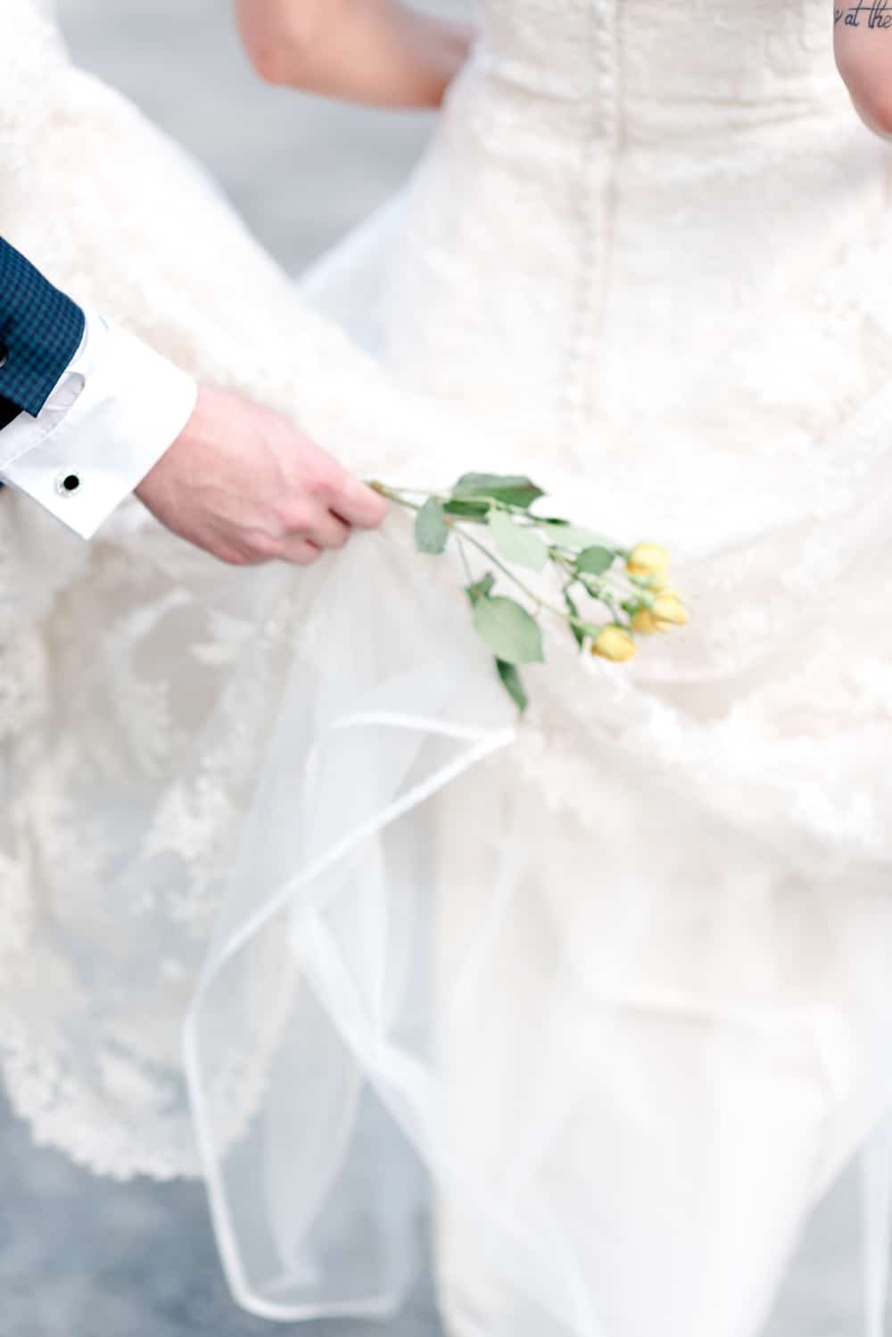 Soft focus image of groom holding flower and bride's gown