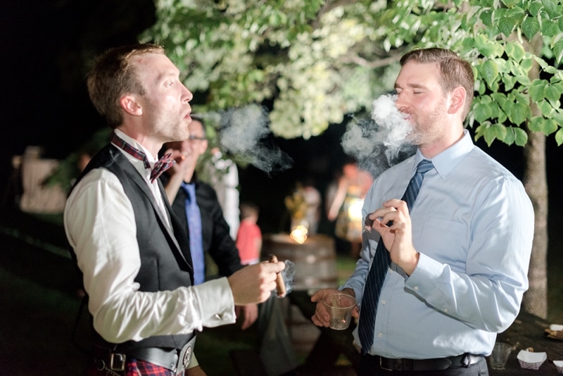 Groom and friend smoking cigars at summer wedding