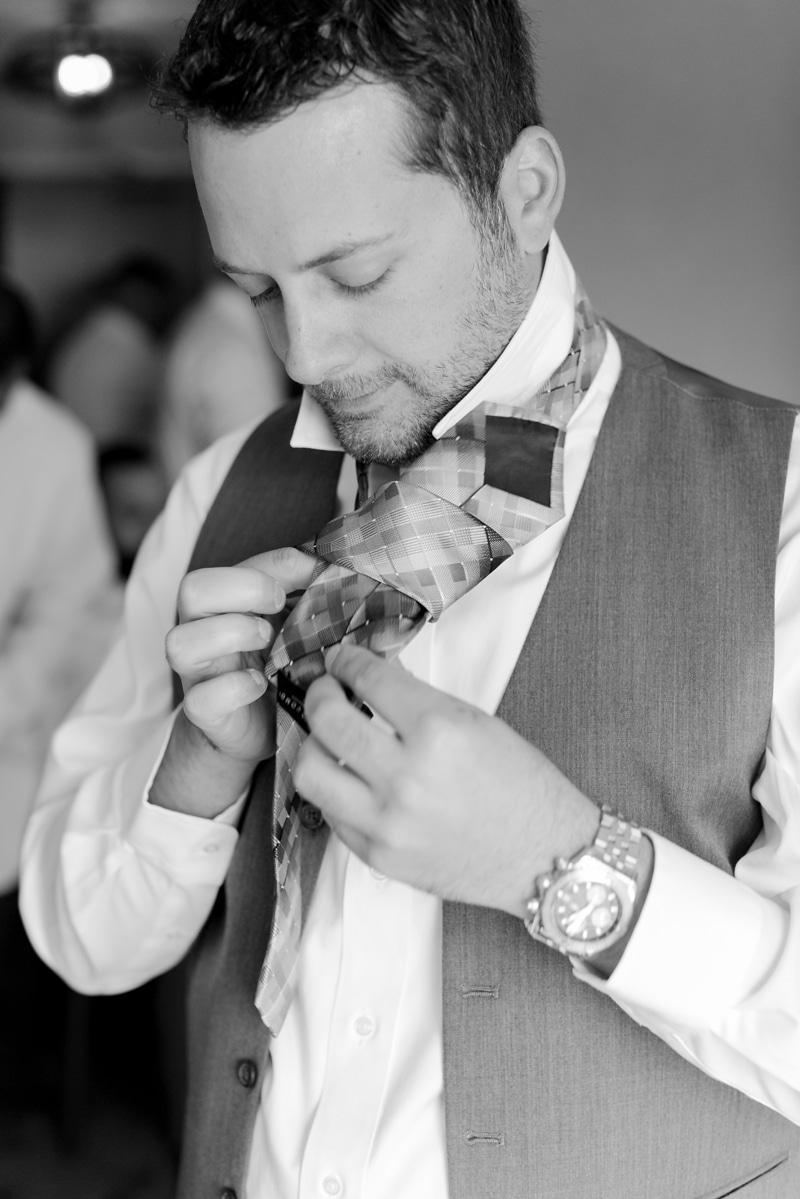 Groom putting on his tie while getting ready for his wedding in MD