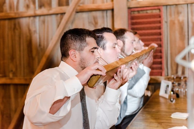 Guests taking shot from shotski at barn wedding