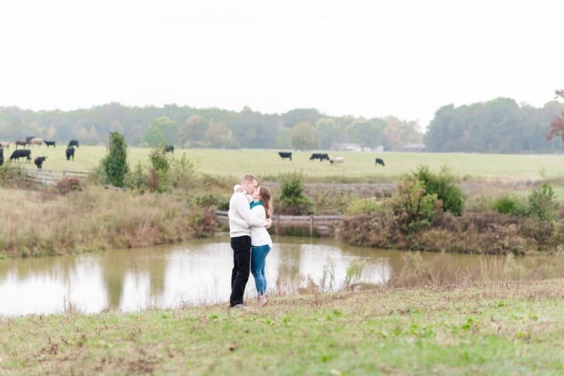 Couple kissing by pond near cows and field